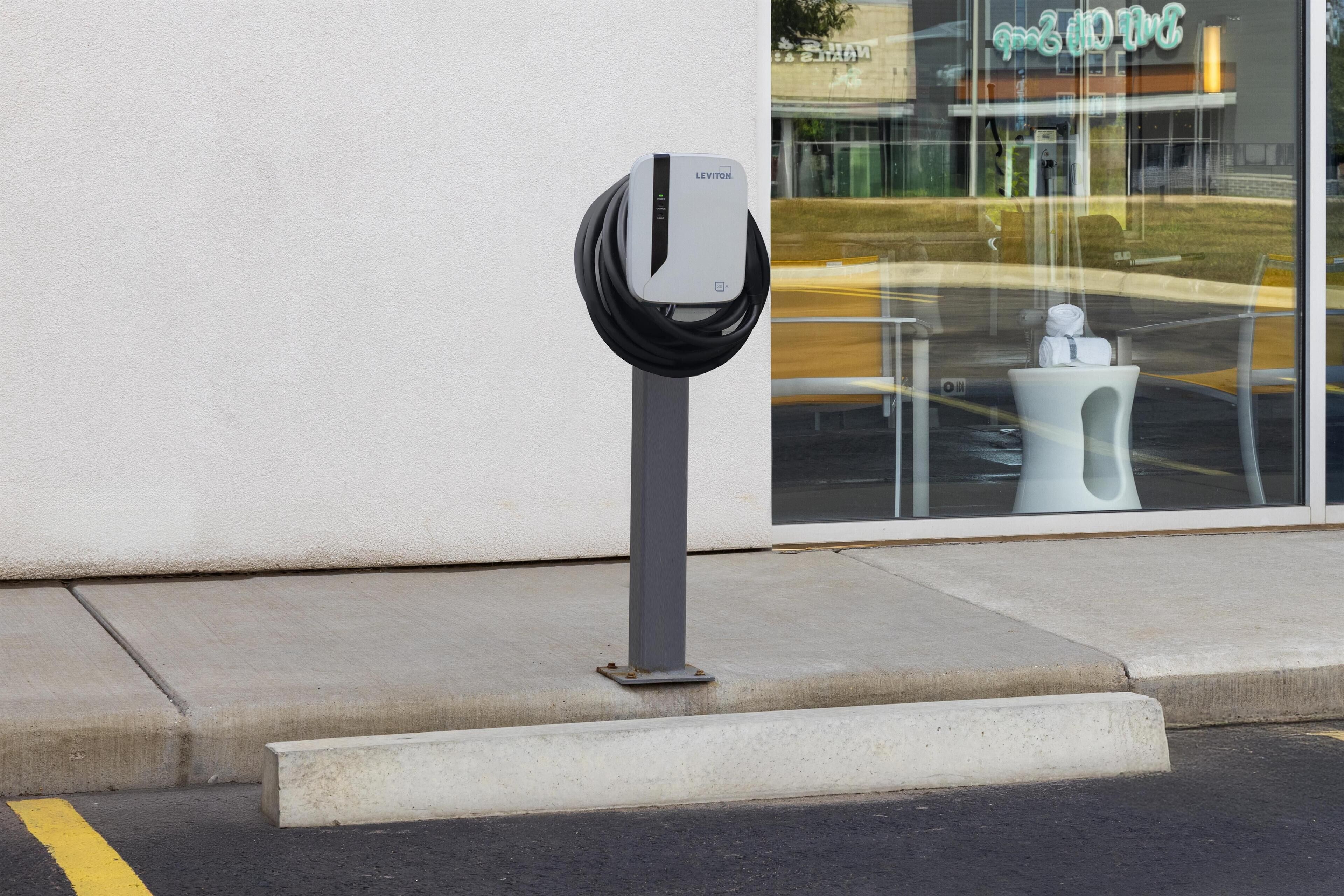 A parking meter with a charging station in front of a building with a glass facade.
