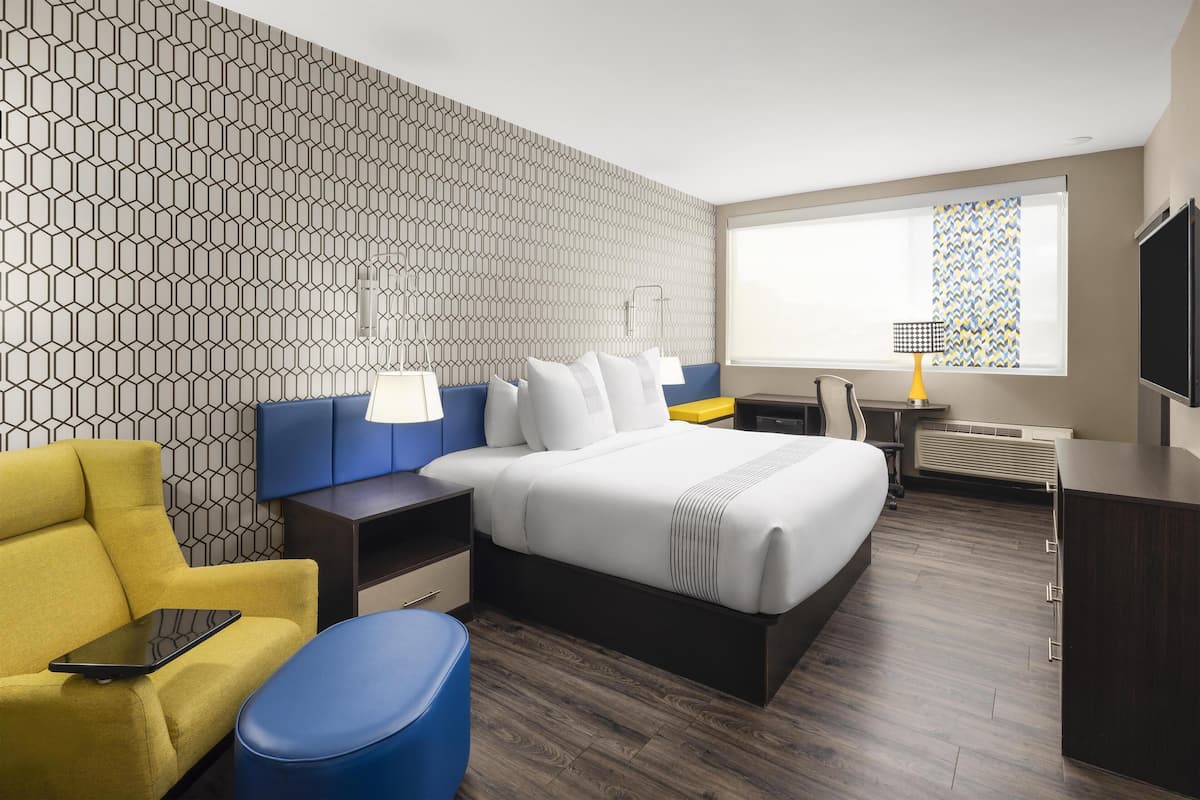 Een moderne hotelkamer met een wand met een geometrisch patroon, een groot bed, een bureau, een gele fauteuil en een televisie.