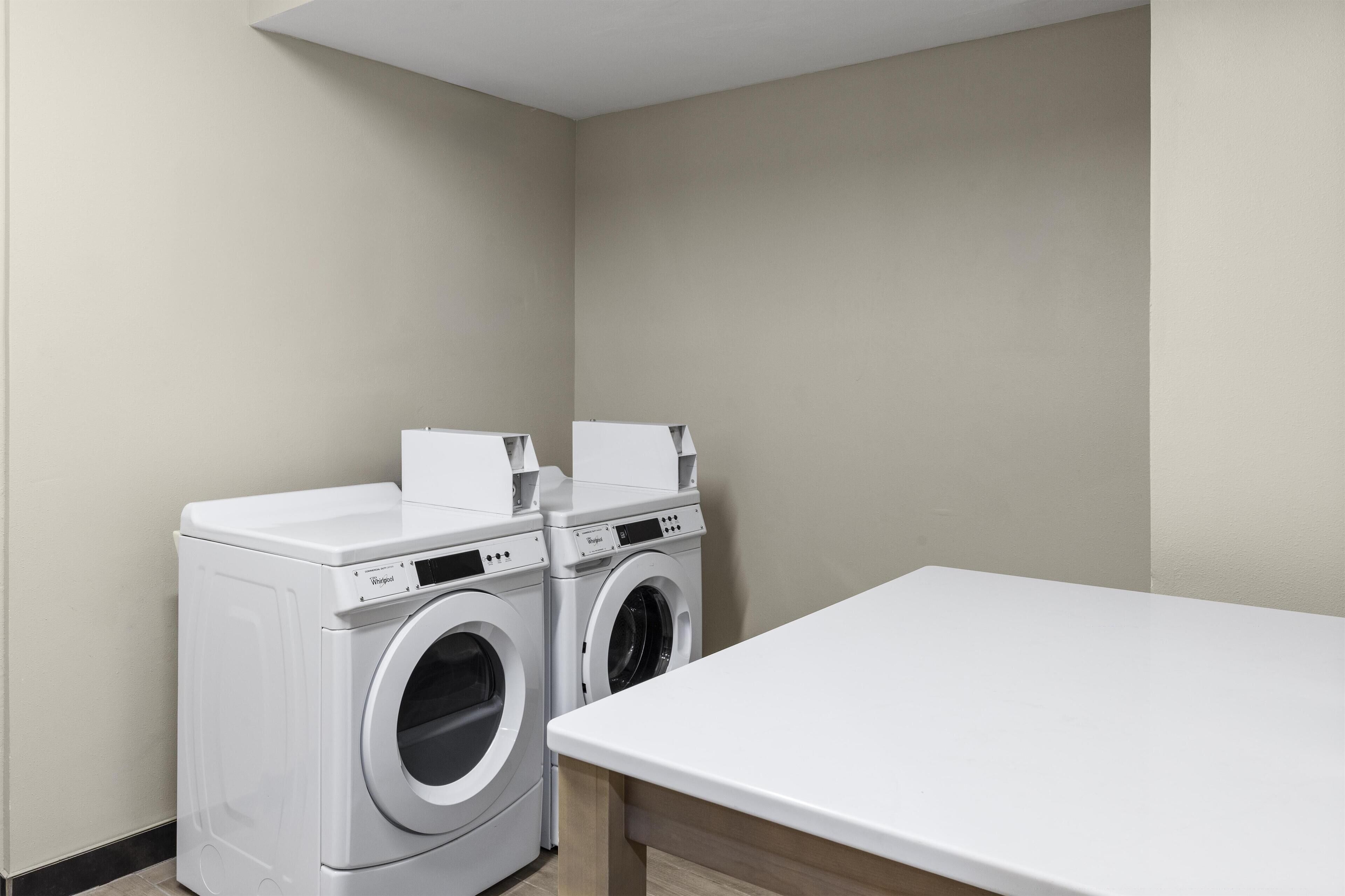 A laundry room with two white front-loading washers and a white table.