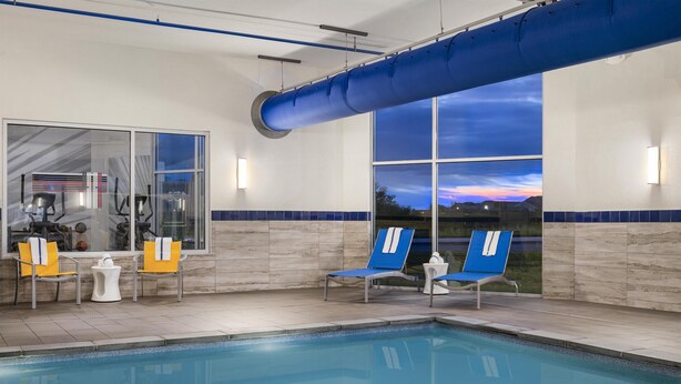 Una piscina con sillas azules, equipo de ejercicios, un gran tubo azul y vistas del atardecer a través de amplias ventanas.