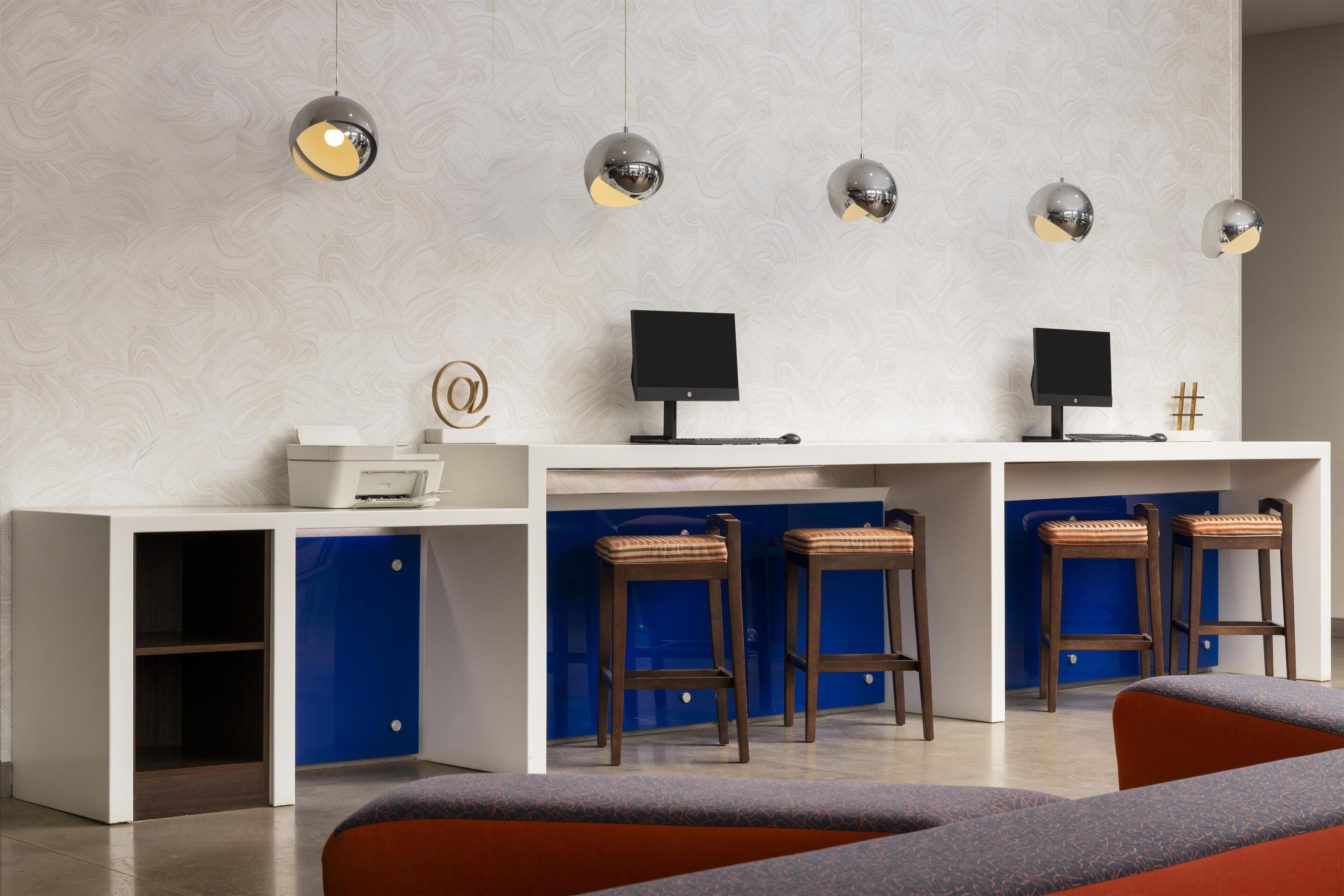 Una moderna zona de recepción con un escritorio blanco, dos monitores y tres taburetes de madera.