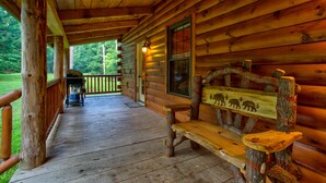 Una baita di legno con veranda, una panca decorata con intagli di animali e un barbecue all'esterno.