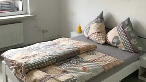A modern bedroom with a bed, a window with a view, a framed picture on the wall, and a bedside table with a lamp. - Eversberg1 - Apartment/ Assembly Meschede-Eversberg (Meschede)