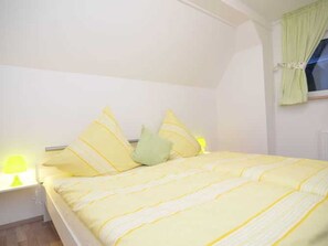 Una cama con ropa de cama amarilla, una almohada verde y una mesita de noche con una lámpara.