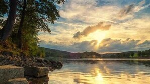 A calm lake with a sunset, trees, and a rocky shoreline. - Eversberg1 - Apartment/ Assembly Meschede-Eversberg (Meschede)