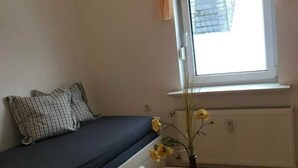 A small room with a bed, a window with curtains, a table with a vase, and a radiator. - Eversberg1 - Apartment/ Assembly Meschede-Eversberg (Meschede)