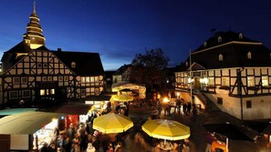 Una plaza tradicional europea de noche, con edificios históricos, una aguja de iglesia y una zona de mercado.
