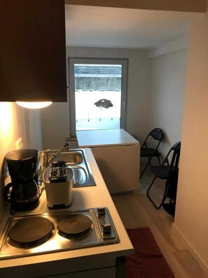 Una kitchenette compacta con cafetera, tostadora, lavamanos y ventana con vista a un estacionamiento.