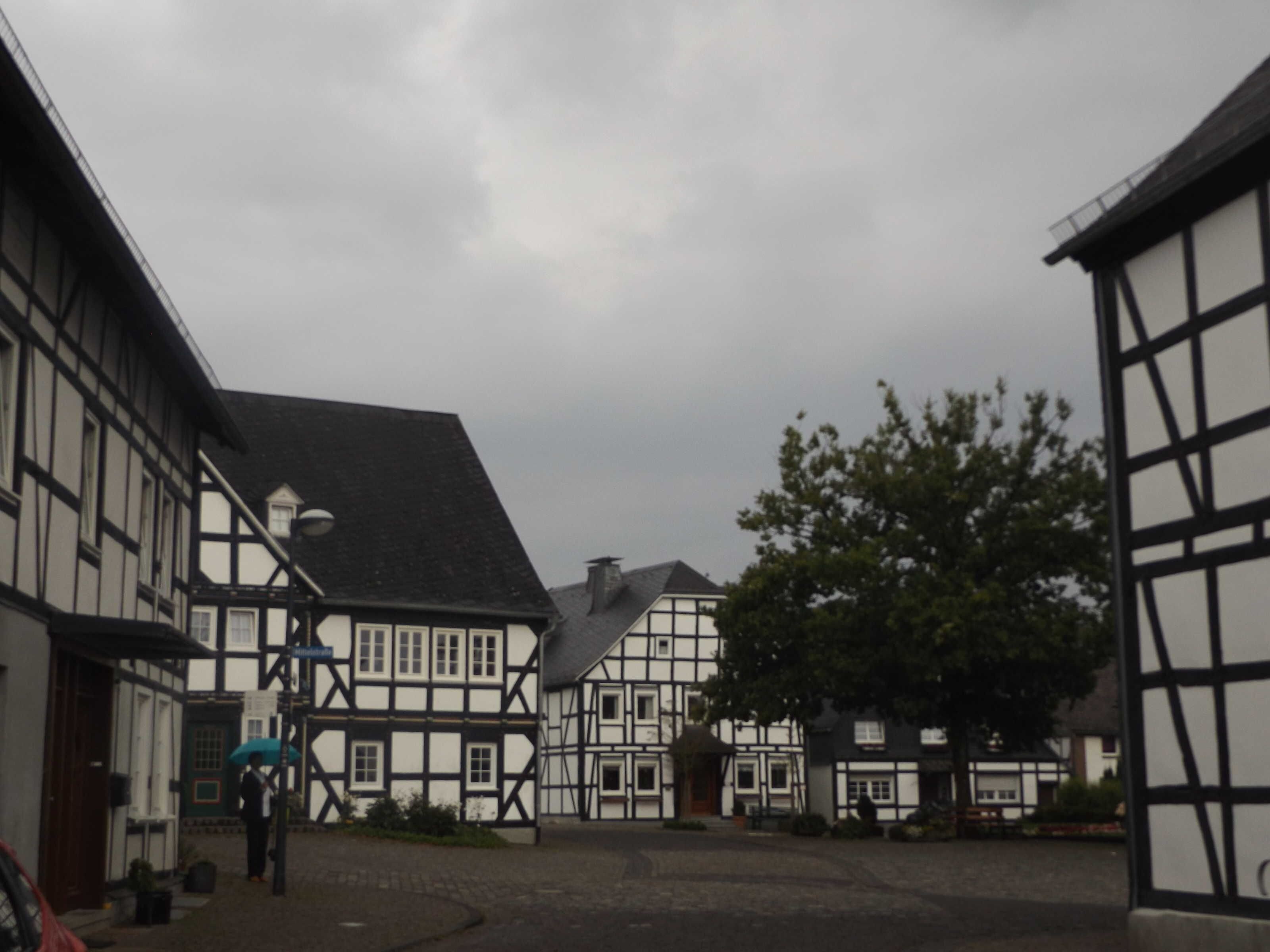 Un bâtiment traditionnel à colombages, avec une rue pavée et une personne tenant un parapluie.