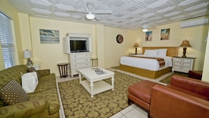 A hotel room with a bed, a sofa, a TV, a ceiling fan, and a small table.