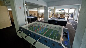 A room with a foosball table, a pool table, and a bar area with chairs.