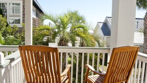 A wooden rocking chair on a wooden deck with a white railing, overlooking a residential area with houses and palm trees.