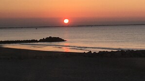 A sunset over a calm sea with a rocky shoreline and a distant cityscape. - Nice air-conditioned studio - wifi - sea view and direct beach access (Palavas-les-Flots)
