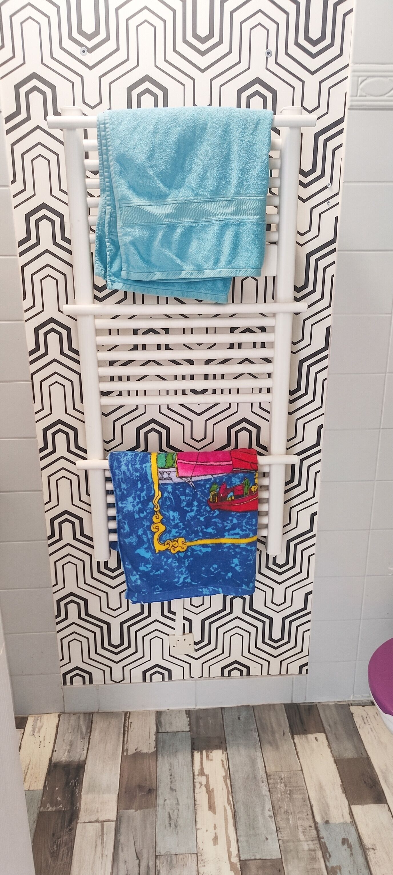 Une salle de bain avec un mur à motifs, un radiateur blanc et un plancher en bois.