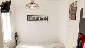 A compact room with a bed, a small kitchenette, a radiator, a ceiling light fixture, and a poster on the wall. - Homerez - Studio with parking in Montargis (Montargis)