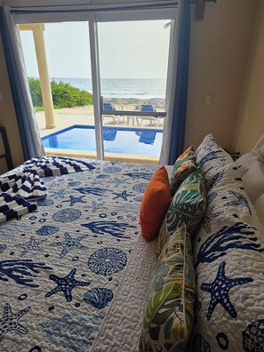 Une chambre avec un lit, une vue sur l’océan par une grande fenêtre et une piscine à l’extérieur.