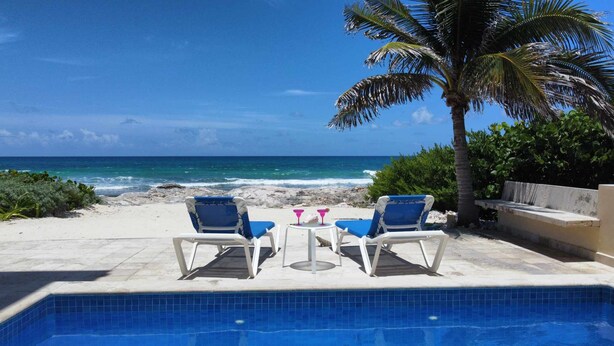 Un espace aménagé au bord de la piscine, avec deux chaises longues et une table, offrant une vue sur la plage et l’océan.