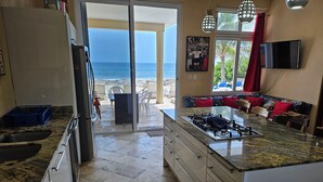 Une cuisine avec vue sur la plage, un coin repas avec un canapé et un téléviseur fixé au mur.