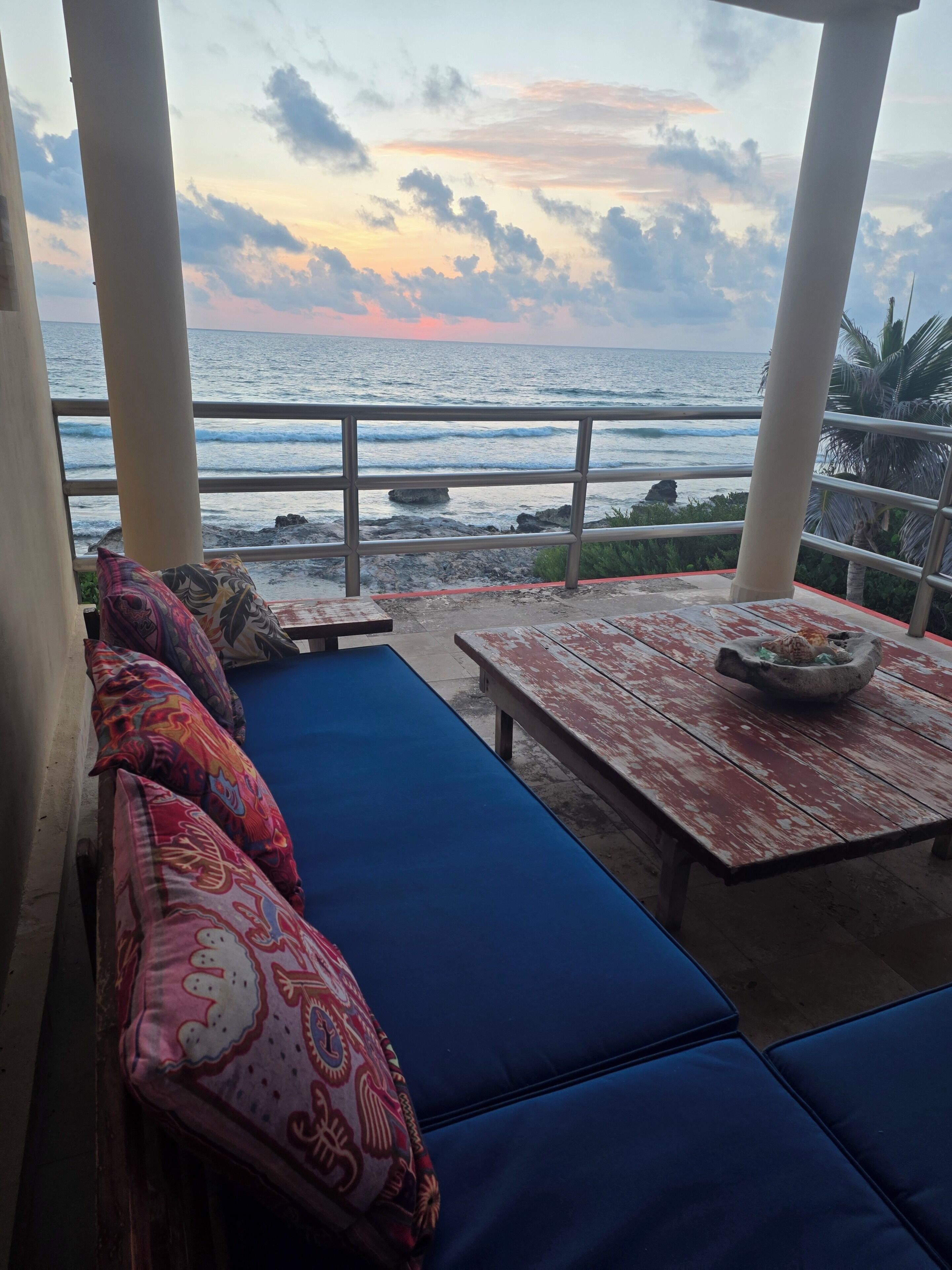 An outdoor seating area with a view of the ocean, featuring a bench and a table with a bowl.