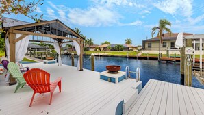 A wooden deck with colorful Adirondack chairs, a hot tub, and a view of a water body with buildings in the background.