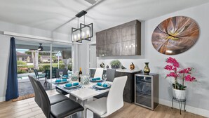 A modern dining area with a white table set for four, black and white chairs, a pendant light, and a large abstract painting on the wall.