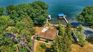 Vue aérienne d’une propriété au bord du lac, avec une maison, un quai et les arbres environnants.