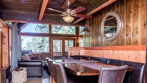 A wooden interior with a round table and leather seating, large windows, and a ceiling fan.