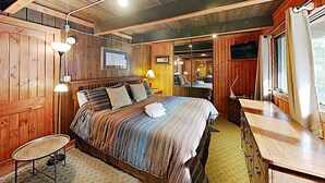 A wooden cabin-style bedroom with a bed, bedside lamps, a small table, and a TV.