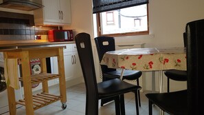 A kitchen with a microwave, a wooden cart, and a table with a floral tablecloth.