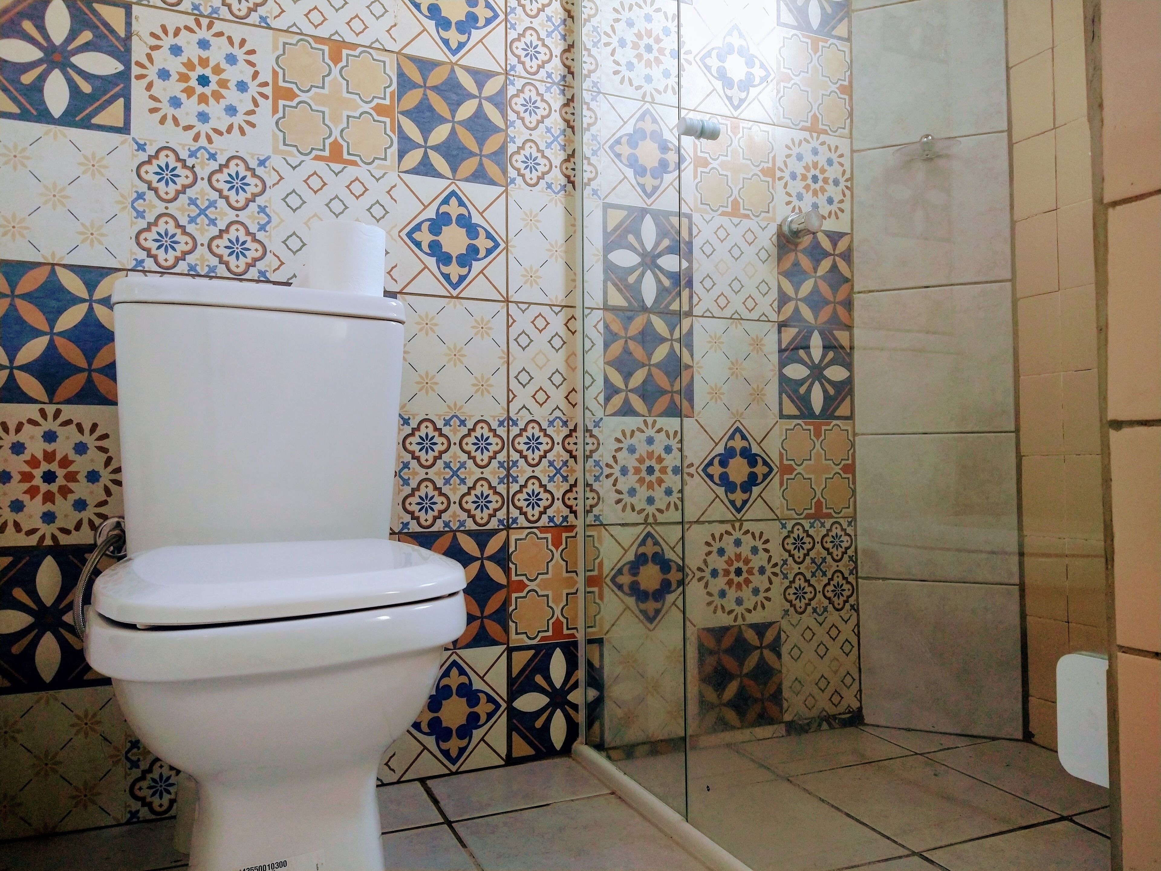 Un baño con inodoro, azulejos estampados y zona de ducha.