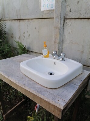 A white sink with a soap dispenser on a wooden table, set against a concrete wall. - Monteverde Eco Love (Monteverde)
