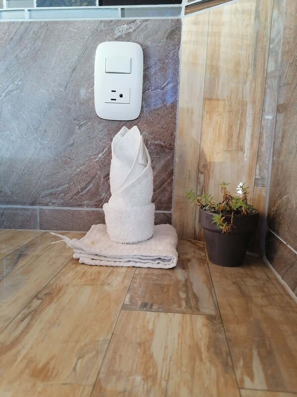 A bathroom with a marble wall, a towel rack with a folded towel, a potted plant, and a power outlet. - Monteverde Eco Love (Monteverde)