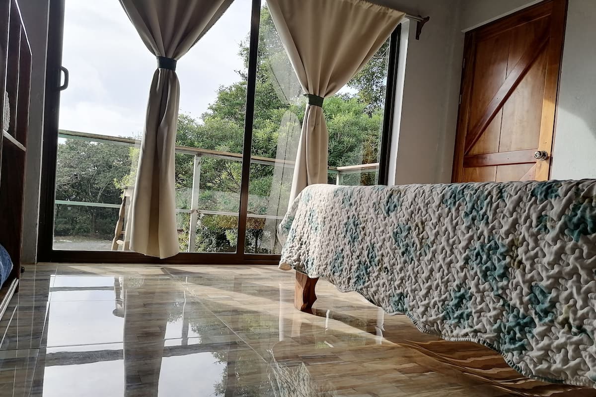 Ein Zimmer mit großem Fenster, Holztür und einem Bett mit gemustertem Überwurf.