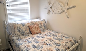 A bedroom with a bed featuring a nautical-themed bedspread, a decorative starfish wall art, and a window with blinds.