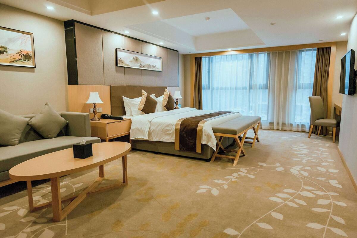 Une chambre d’hôtel avec un lit, un canapé, une petite table, une table de chevet et un téléviseur.