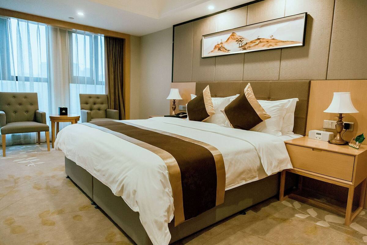 Une chambre d’hôtel avec un grand lit, deux tables de chevet avec des lampes, une chaise et un tableau au mur.