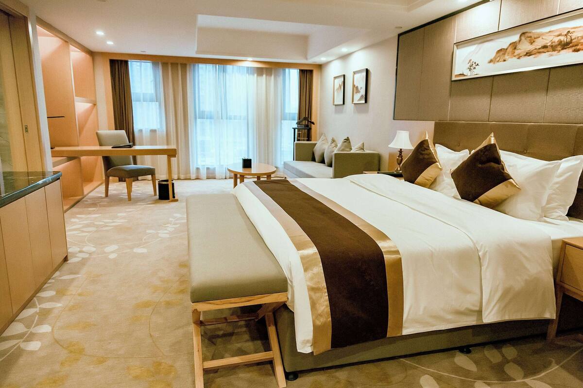 Une chambre d’hôtel avec un grand lit, un bureau, une chaise, un canapé et une petite table.