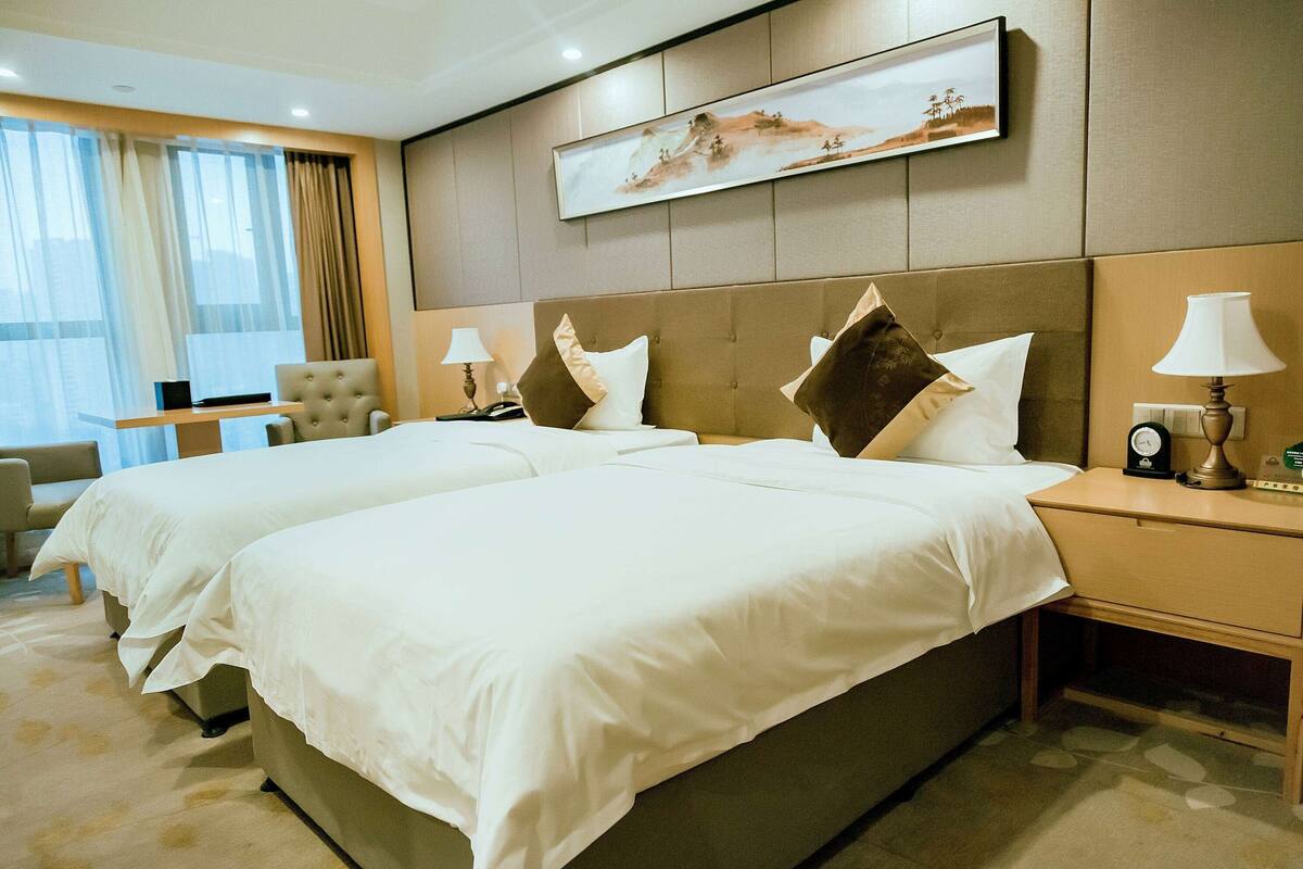 Une chambre d’hôtel avec deux lits, un bureau, une chaise et un tableau au mur.