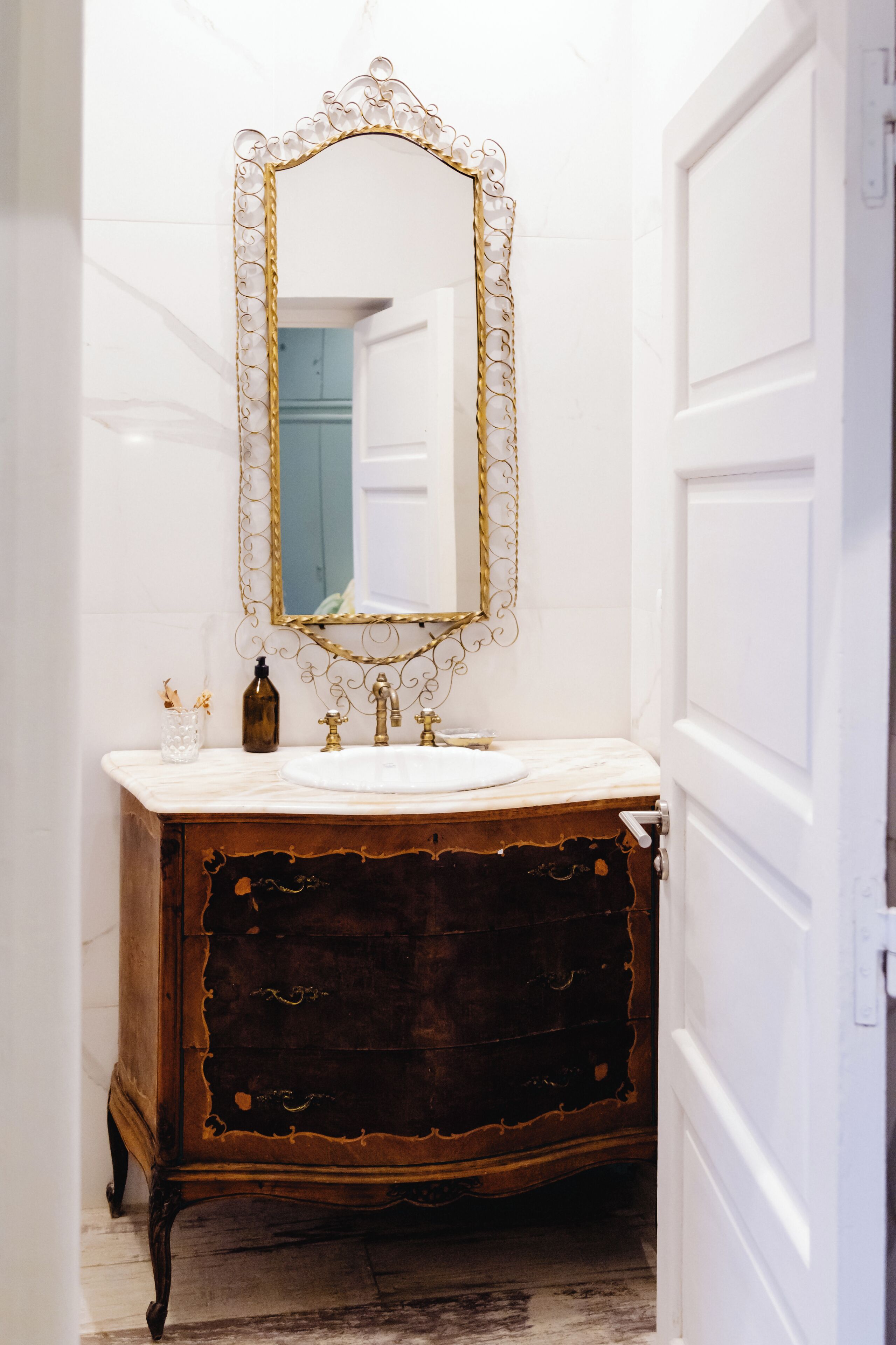 Un baño con lavamanos de mármol, espejo con marco dorado y tocador de madera.