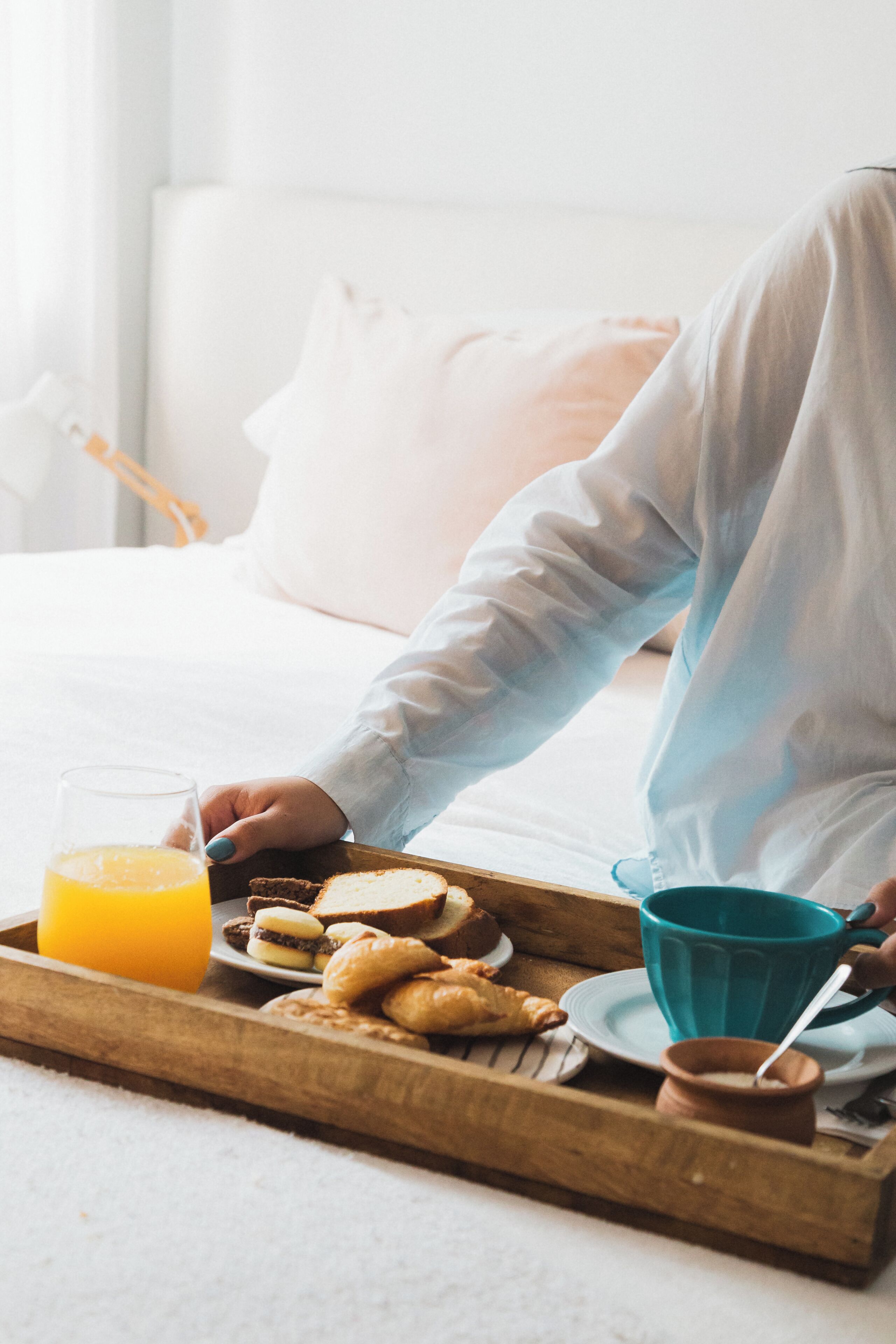 A breakfast tray with croissants, a glass of orange juice, and a blue mug on a wooden tray.