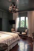 Habitación de hotel con una cama grande, dos sillones, una mesita, un televisor instalado en la pared y un ventanal con cortinas.