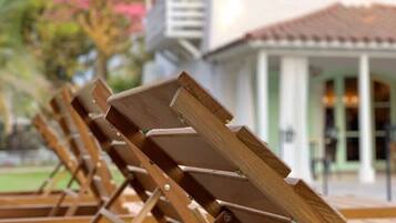 Fileira de cadeiras de madeira com estrutura de metal, dispostas em linha em frente a um edifício com telhado de azulejos e varanda.