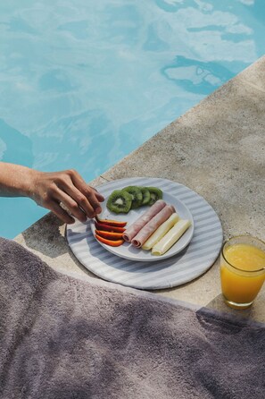 Enjoy a casual meal by the pool, with a refreshing glass of orange juice and a selection of sliced fruits.