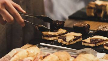 A person serving food, including sandwiches and desserts, on a wooden table.