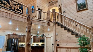 A cabin interior with a wooden staircase, a kitchen area, and a living room with a couch and a decorative pillow. - Imperial Elk Lodge-10 Miles to YNP+Sauna+Hot Tub+Wifi+AC (Island Park)