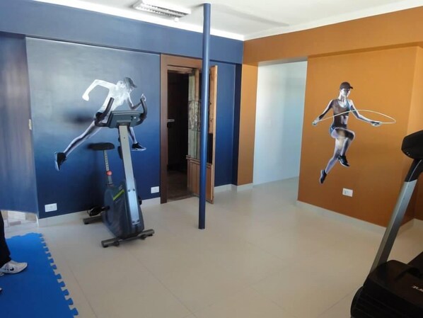Un gimnasio con equipo de ejercicio, incluyendo una cinta de correr y una elíptica, y un mural de una persona saltando la cuerda.