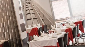 A restaurant with tables set for dining, featuring a modern design with a sloped ceiling and a patterned wall. - Arua Hotel (Presidente Prudente)