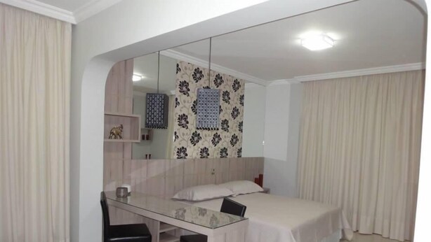 A bedroom with a bed, a desk, and a chair. There is a mirror above the desk and a shelf with decorative items. - Arua Hotel (Presidente Prudente)