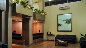 A lobby with a reception desk, a black sofa, a coffee table, and a painting on the wall. - Arua Hotel (Presidente Prudente)