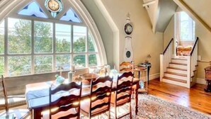 Ein Essbereich mit einem Tisch für vier Personen, einer Holztreppe und einem großen Bogenfenster mit einer Uhr.